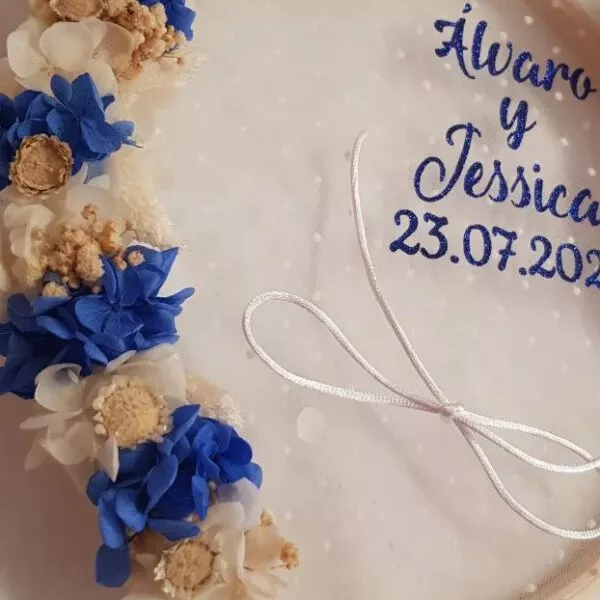 Bastidor porta alianzas de madera con flores preservadas azul marino y crema y nombres bordados en azul