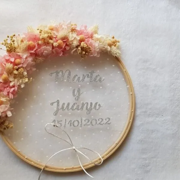 Bastidor porta alianzas de madera con arco superior de flores rosa suave y crema y texto personalizado de boda
