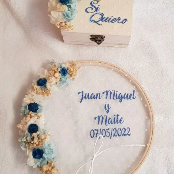 Bastidor porta alianzas de madera con flores azules preservadas y nombres bordados en azul para boda