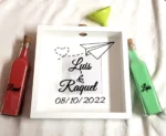 Cuadro ceremonia de la arena con diseño de avión de papel y mensaje romántico. Un detalle único para bodas con tema de viaje o amor a distancia.