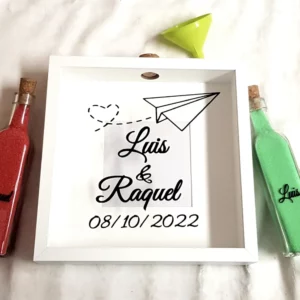 Cuadro ceremonia de la arena con diseño de avión de papel y mensaje romántico. Un detalle único para bodas con tema de viaje o amor a distancia.