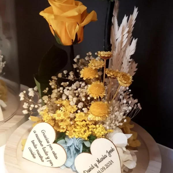 Cúpula de cristal con rosas preservadas azul y amarillo, flores secas y corazones grabados.