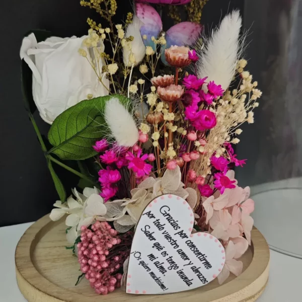 Cúpula de cristal con rosas preservadas en blanco y fucsia, flores secas y corazón de madera grabado.