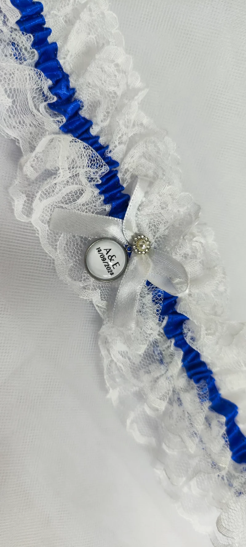 Liga de novia personalizada con encaje blanco, cinta azul y camafeo personalizable.