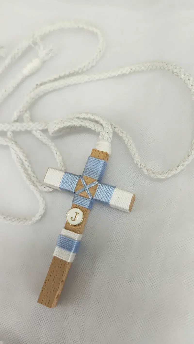 Cruz de comunión para niño en madera con hilo azul y blanco, inicial personalizada y cordón trenzado.