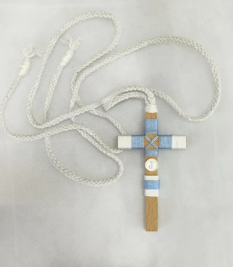 Cruz de comunión para niño en madera con hilo azul y blanco, inicial personalizada y cordón trenzado.