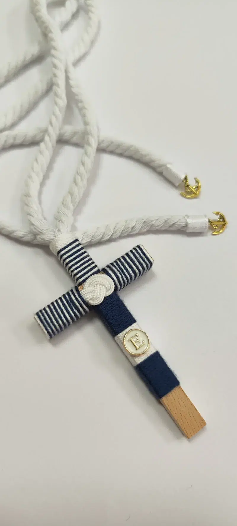 Cruz de comunión en madera con hilo azul marino y blanco, inicial personalizada y cordón retorcido con detalles de anclas doradas.