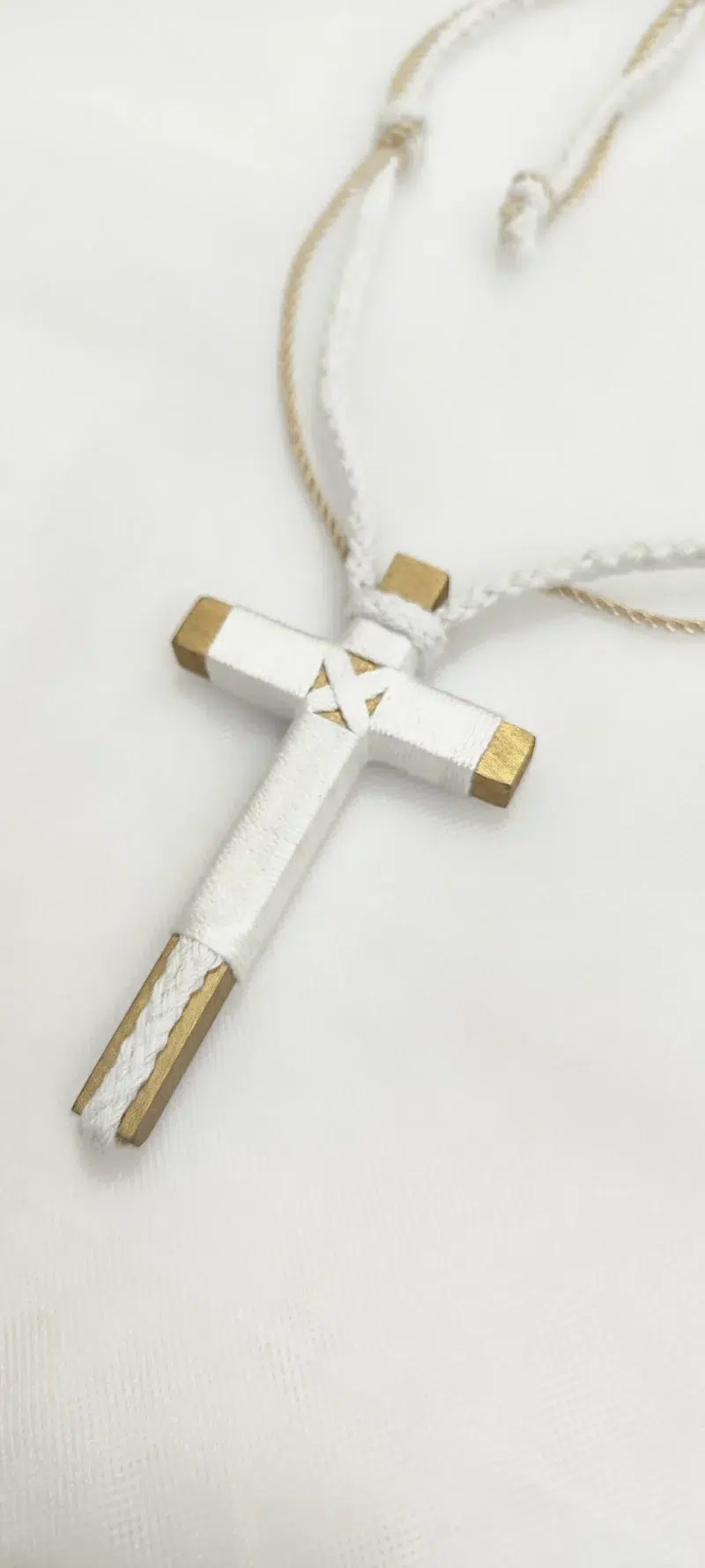 Cruz de comunión en madera con hilo blanco y detalles dorados, cordón ajustable en blanco y beige.