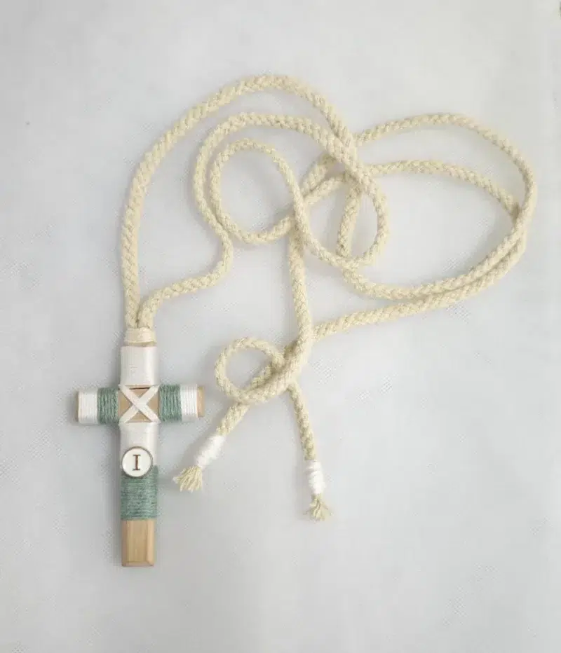 Cruz de comunión en madera con hilo verde y blanco, inicial personalizada y cordón trenzado beige.