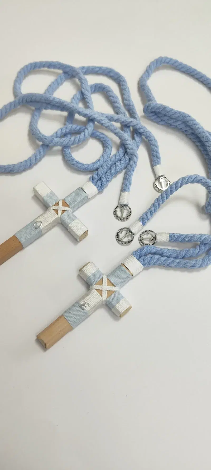 Conjunto de cruces de comunión en madera con hilo celeste y blanco, iniciales personalizadas y cordón trenzado azul con detalles plateados.