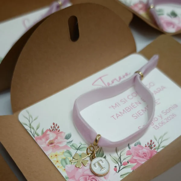 pulsera elástica de terciopelo rosa con inicial dorada y trébol sobre tarjeta personalizada con sobre kraft