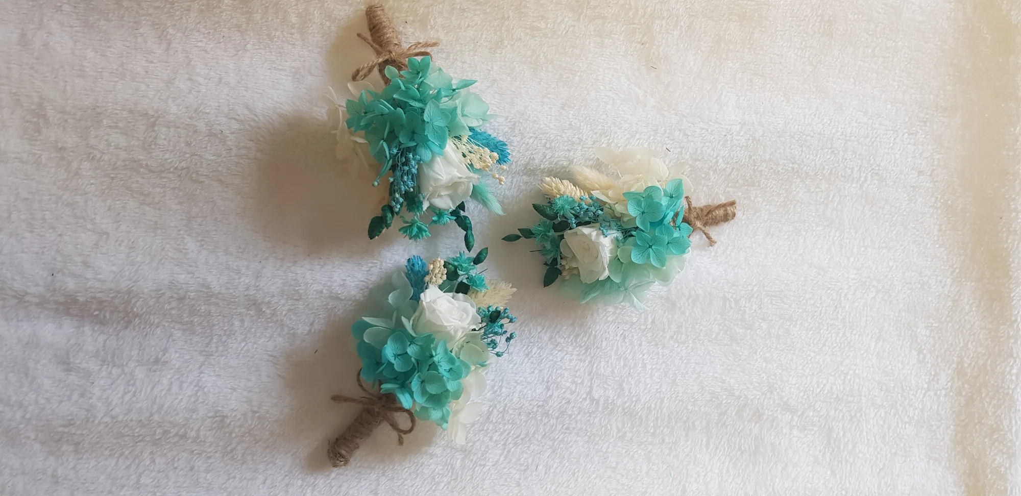 Varios prendidos de novio de flores preservadas turquesa y blanco con tallos envueltos en yute