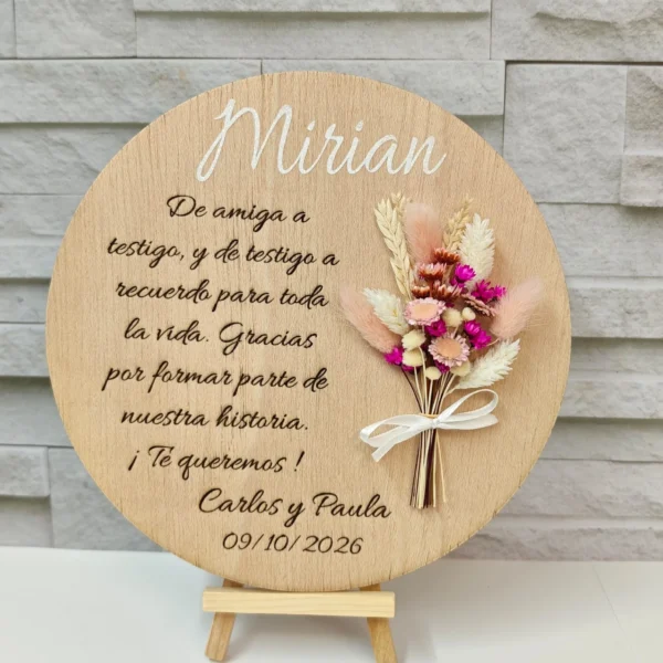 placa de madera redonda con grabado láser, nombre y ramito de flores sobre caballete